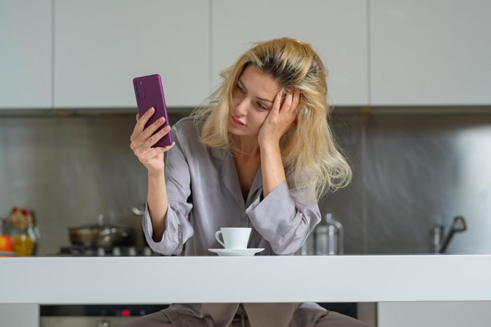 Young woman looking upset while holding smartphone, illustrating sibling cut off and Instagram blocking issues.