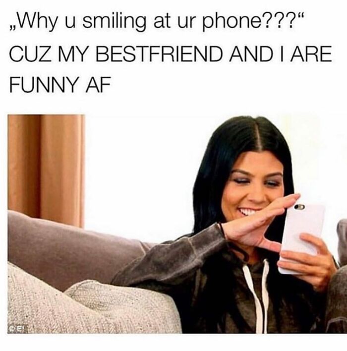 Young woman smiling at her phone, enjoying funny girly memes about friendships and relatable moments.