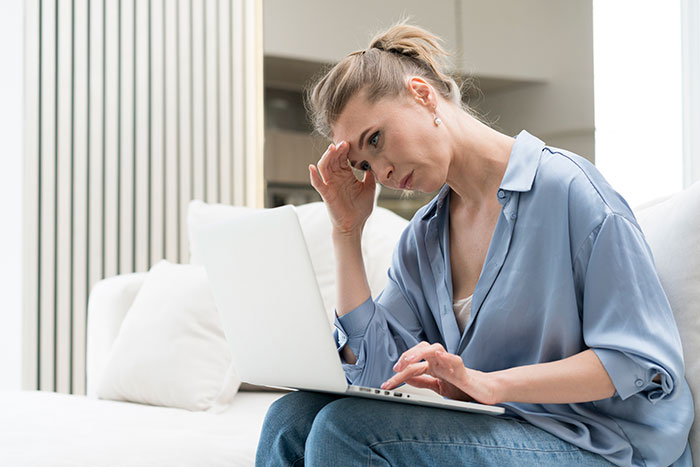Woman looking concerned while using laptop at home, relating to stories about hospital visits and unexpected surgery cases.