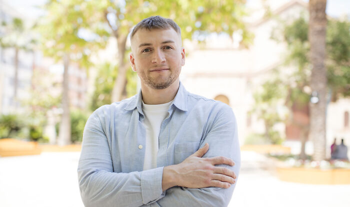 Young man standing outdoors with arms crossed, smiling confidently while highlighting loopholes to take advantage of.