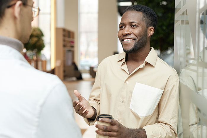 Man holding coffee cup smiling and discussing social cues that confuse people in a modern office setting