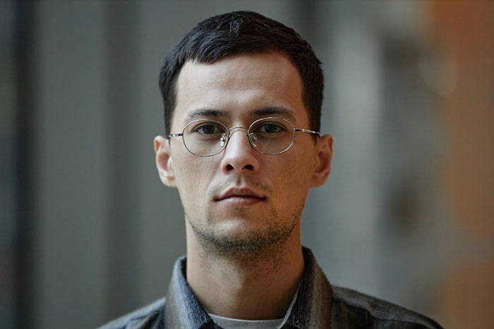 Young man with glasses in a gray shirt looking serious, illustrating social cues that confuse people in interactions.
