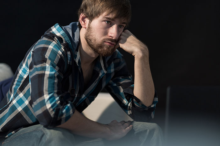 Young man in a plaid shirt showing confusion, illustrating challenges with understanding social cues in a dimly lit room.