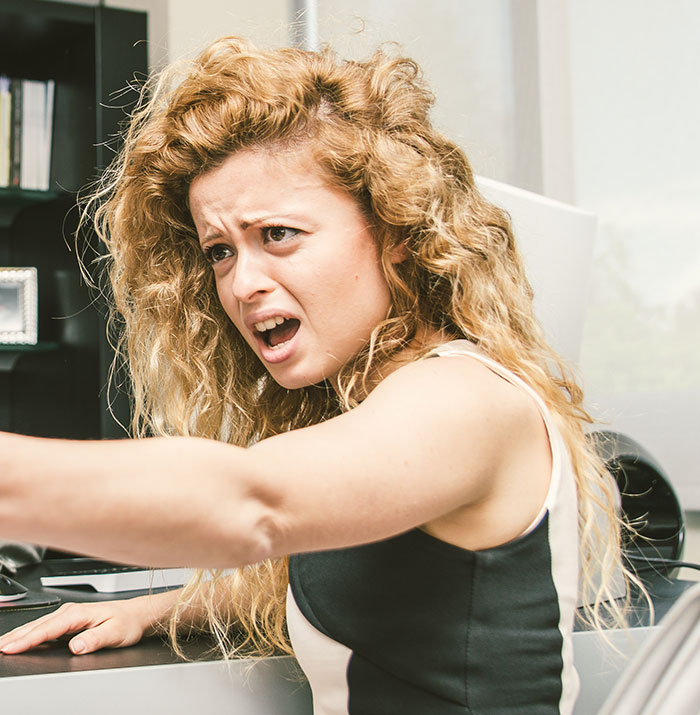 Young woman showing confusion and frustration with social cues while sitting at a desk in an office setting.