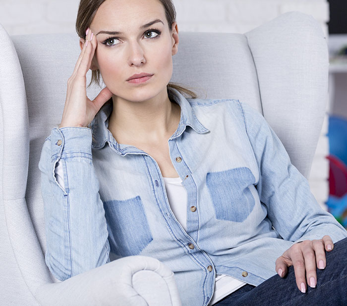 Young woman sitting in armchair, appearing confused and thoughtful, illustrating social cues confusion.