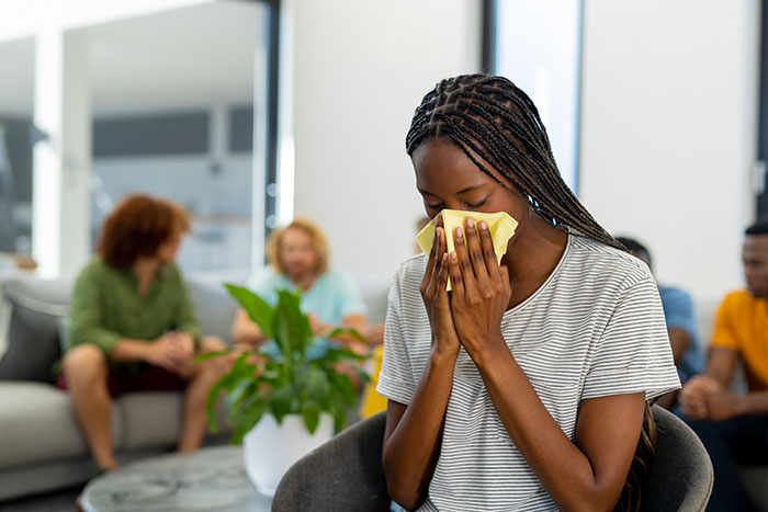 Young woman wiping nose with tissue in a group setting, illustrating social cues that confuse people during interactions.