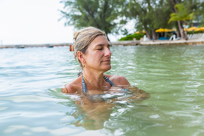 Woman with eyes closed in water near shore reflecting on confusing social cues and body language outdoors.