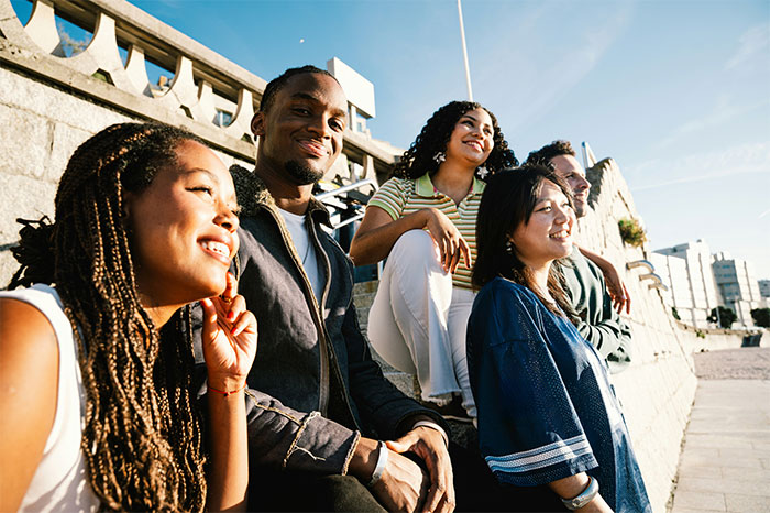 Group of diverse friends with high social skills sitting outdoors, enjoying conversation and positive social interaction in sunlight.
