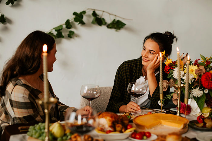 Two women with high social skills sharing a conversation over dinner with wine and candles in a cozy setting.