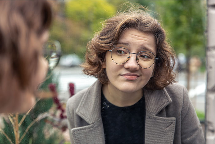 Young woman with glasses showing social skills, engaging in a reflective conversation outdoors near a window.