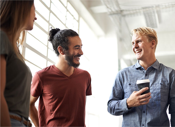 Three people with high social skills having a lively conversation near a window in a bright indoor setting.