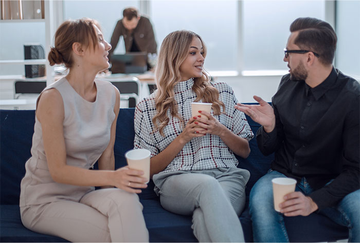 Three people with high social skills holding coffee cups, engaging in an active conversation on a couch.