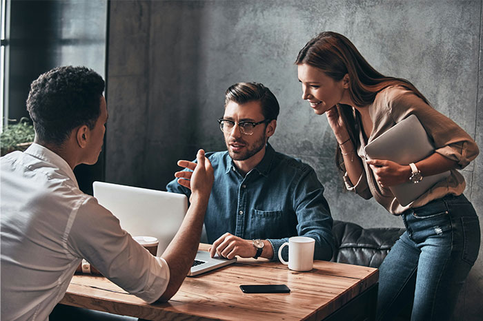 Three young professionals with high social skills having a conversation in a modern office setting.