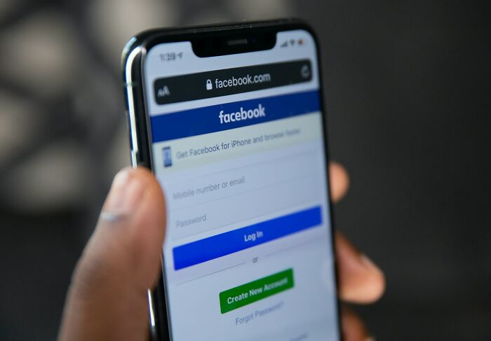 Close-up of a hand holding a smartphone showing the Facebook login screen, illustrating strange and dumb health hacks.