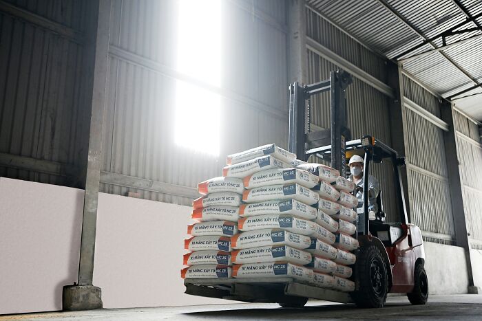 Forklift operator wearing mask loads cement bags in a warehouse.