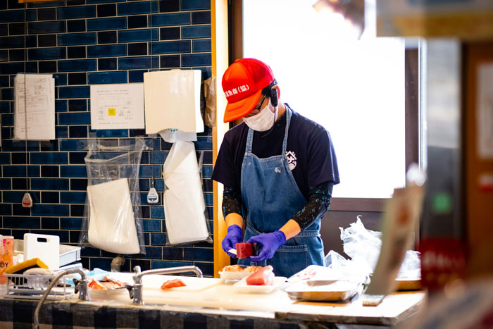 Young adult working in a kitchen wearing a mask and gloves, representing a 20YO mooching off parents scenario.