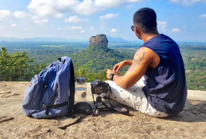 Young man with backpack and camera enjoying scenic travel view, illustrating consequences of spending college money on traveling.