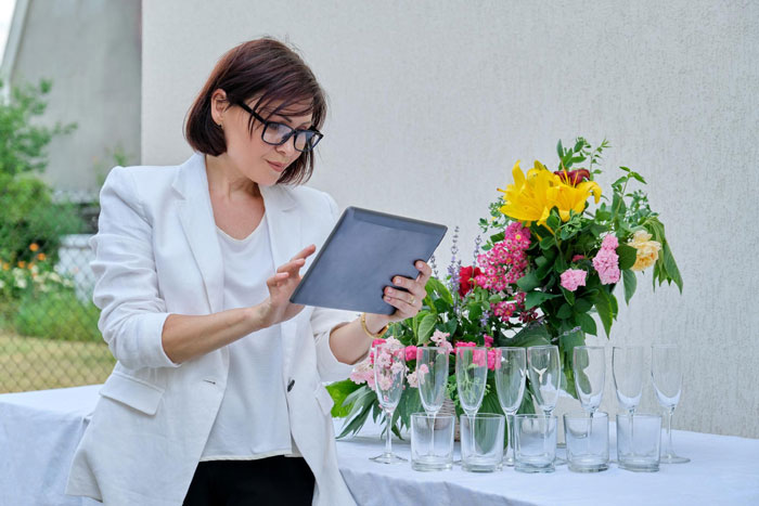 Woman in white blazer using tablet near wedding table with flowers and glassware, capturing Star Wars wedding preparations.