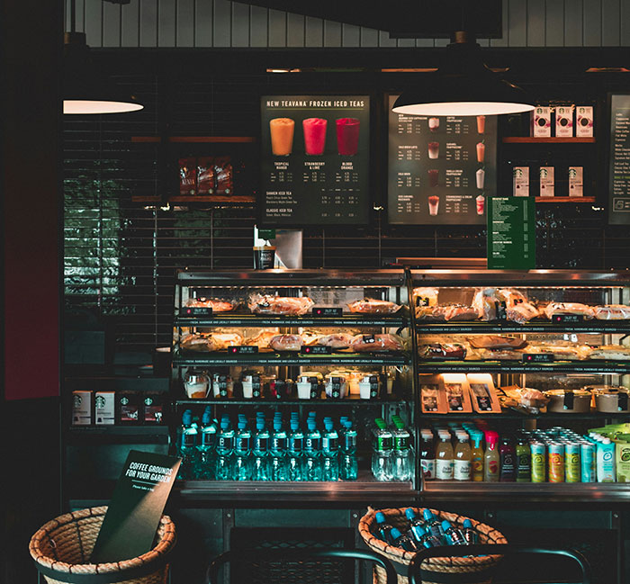 Starbucks interior showing display case with pastries, drinks, and menu board highlighting Florida man incident over pride flag.