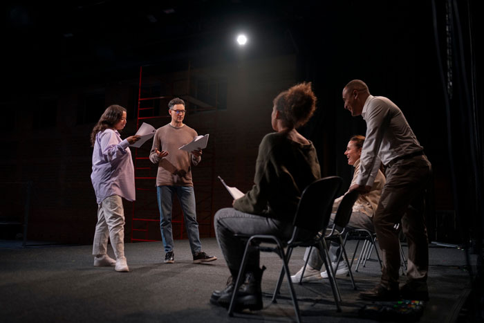 Group of actors rehearsing on stage under spotlight, focused on steering career against dreams in performing arts.