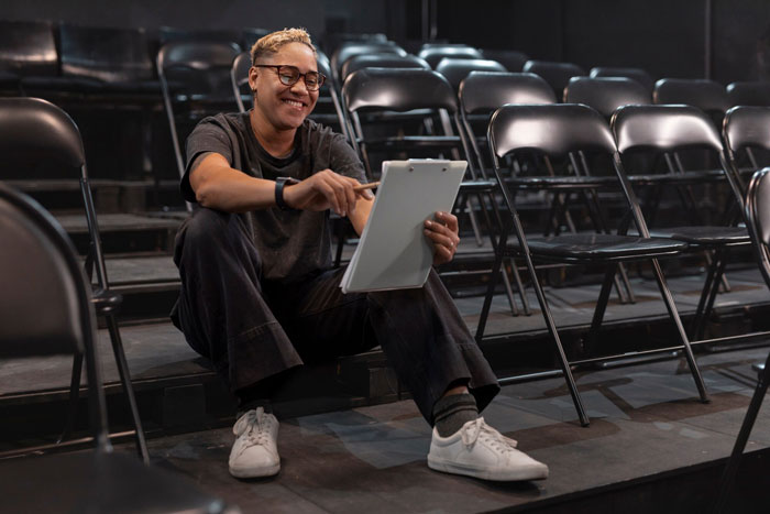 Person reviewing notes on a tablet, smiling while seated among empty chairs, focusing on steering career against dreams.