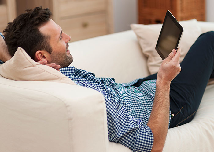 Step-dad lying on couch looking at tablet, reflecting on heartbreaking moment with girlfriend and her daughter.