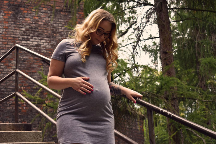 Pregnant woman in gray dress standing on outdoor stairs, symbolizing mom poisoning kids against stepmom conflict.