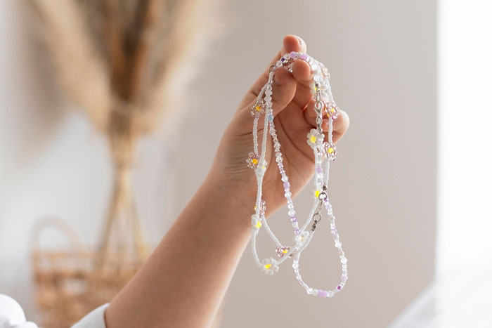 Hand holding delicate heirloom jewelry with beads and flower charms, symbolizing valuable $100k family heirloom conflict. Hand holding delicate heirloom jewelry with beads and flower charms, symbolizing valuable $100k family heirloom conflict.