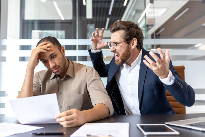 Frustrated boss angrily yelling at stressed worker holding paper, illustrating toxic bosses and hostile work environment.