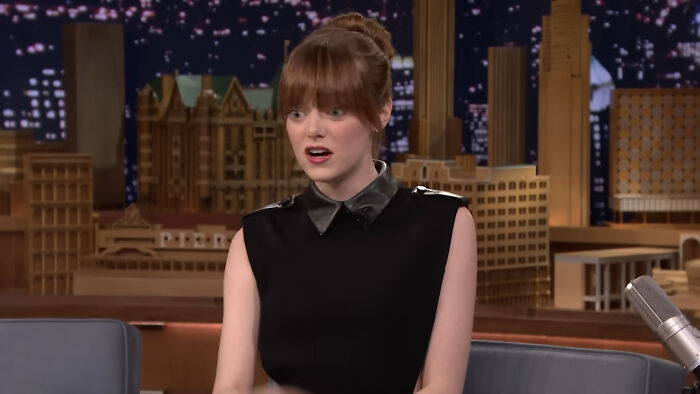 Actress in a black dress reacting with surprise during a late-night talk show about bizarre things found inside strangers’ houses.