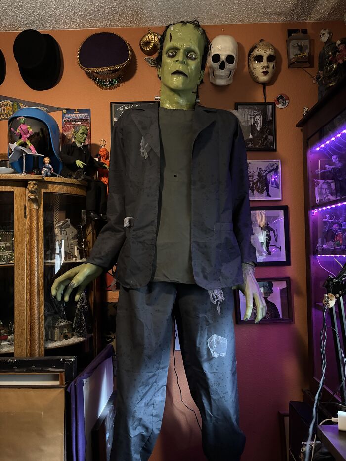 Life-size Frankenstein figure inside a strange house surrounded by horror collectibles and masks, bizarre things found indoors.