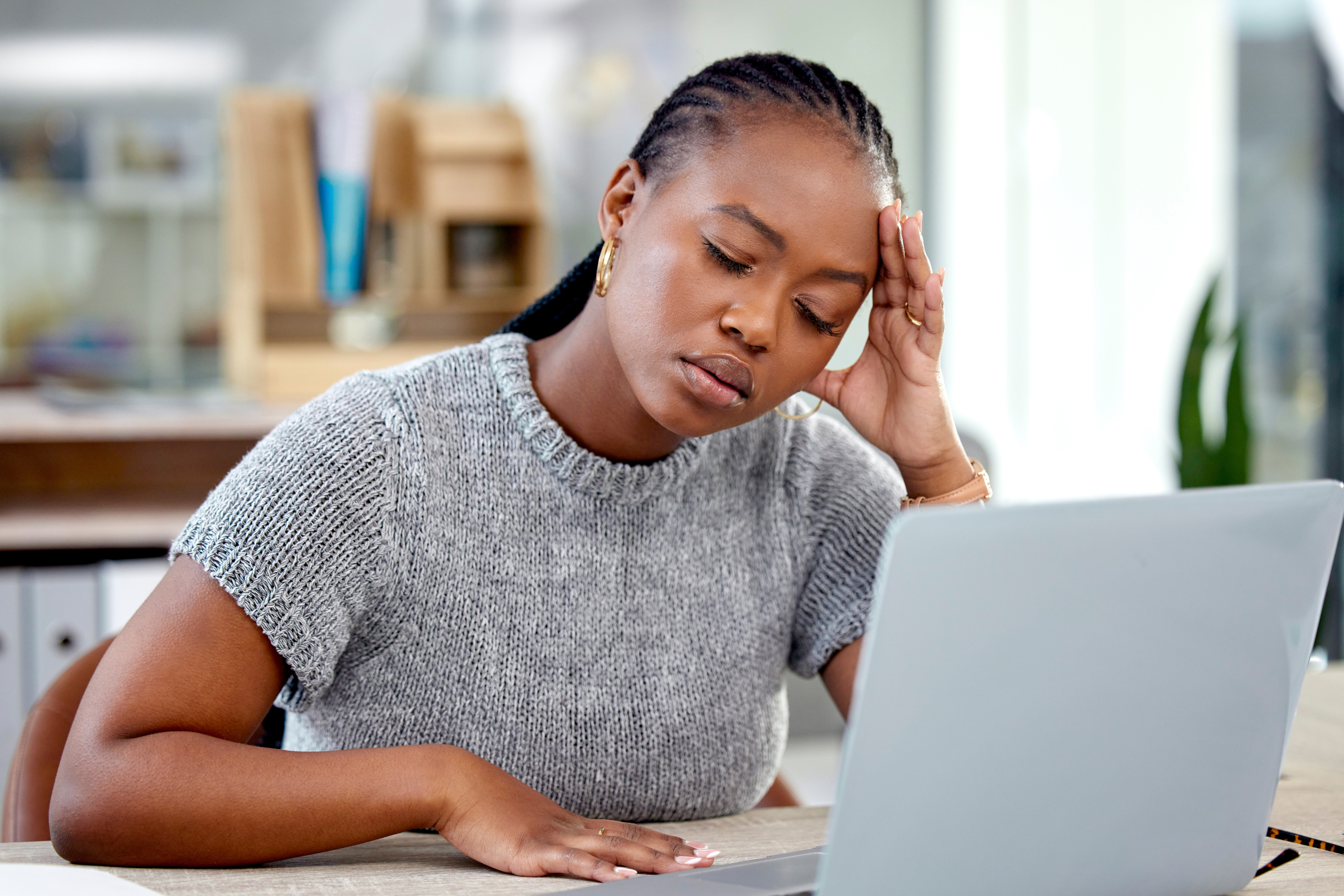 African American woman looking stressed while working on a laptop, highlighting issues of job offers and name bias.