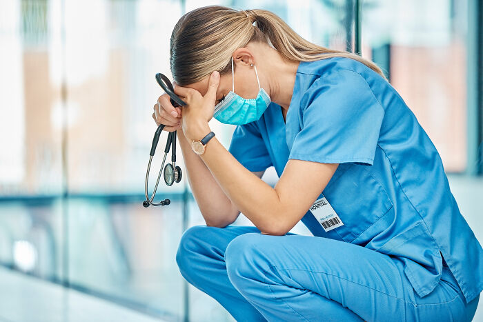 Stressed female doctor in blue scrubs wearing a mask, holding a stethoscope, overwhelmed by worst first opinions heard.