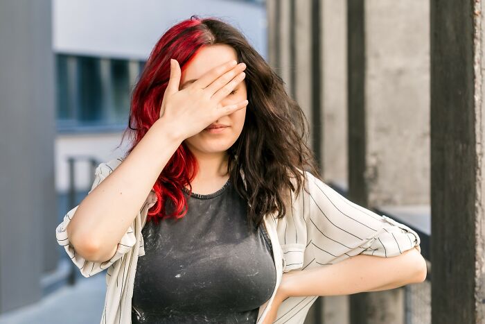 Woman with red and black hair covering her eyes, expressing discomfort related to medical problems that are worse than people think.