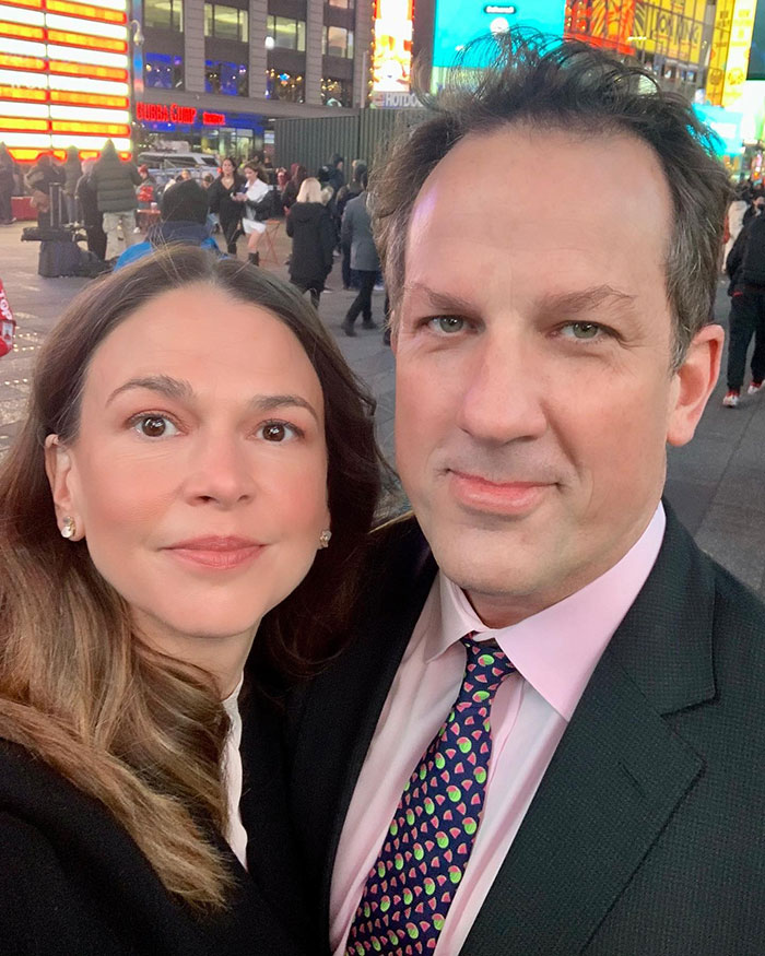 Man and woman taking a close-up selfie in a busy urban setting, reflecting a midlife crisis on the red carpet.