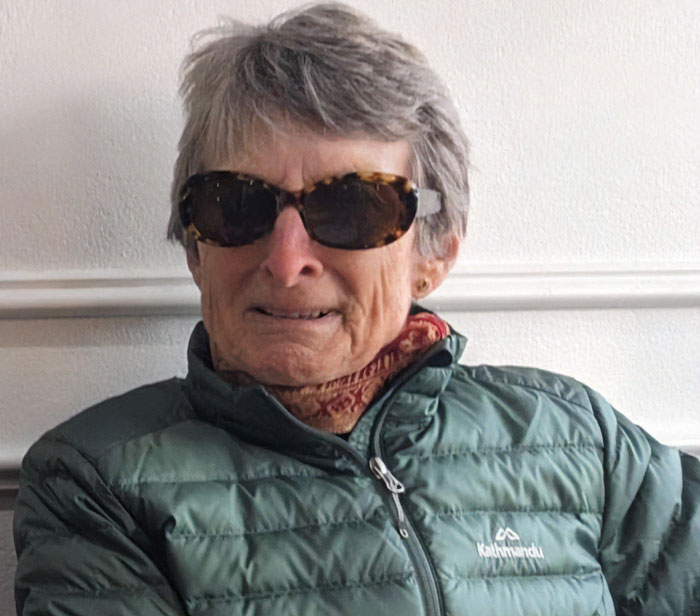 Elderly woman in sunglasses and green jacket, revealing final moments after being stranded on remote island by cruise ship