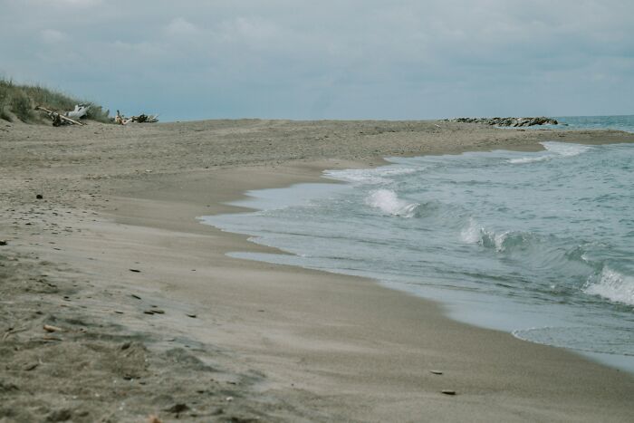 Empty sandy ocean shore with gentle waves under a cloudy sky, showing a calm and fascinating ocean scene.