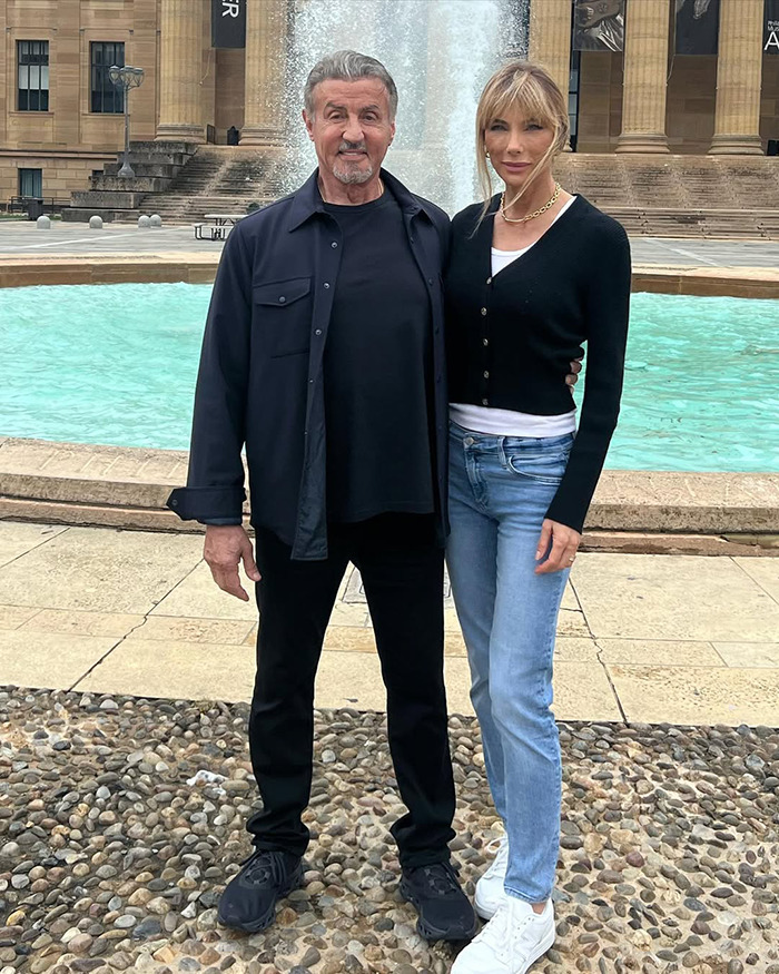 Sylvester Stallone and his wife standing near a fountain, relating to trans nepo babies controversy in Hollywood.
