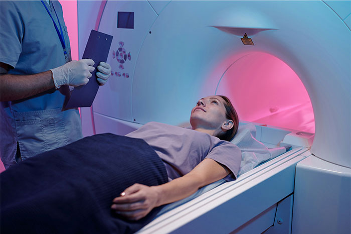 Patient undergoing MRI scan watched by doctor holding clipboard, illustrating symptoms that led to cancer diagnosis.