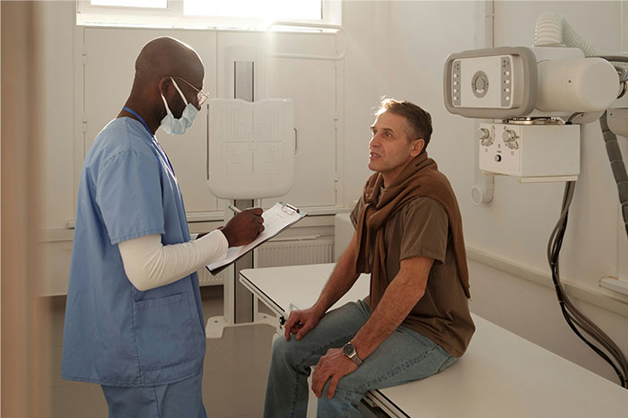 Doctor in scrubs discussing cancer symptoms with a patient in a medical exam room during consultation.