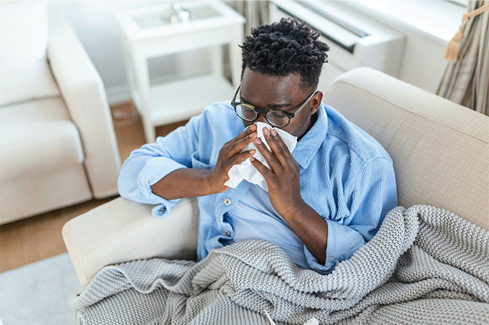 Man sitting on couch with blanket, blowing nose, illustrating symptoms that made people see a doctor for cancer diagnosis.
