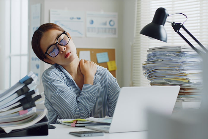 Woman at cluttered desk holding shoulder in discomfort, illustrating symptoms that made people see a doctor for cancer diagnosis