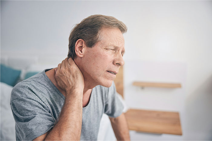 Middle-aged man with gray hair holding neck in pain, illustrating symptoms that made people see a doctor for cancer diagnosis.