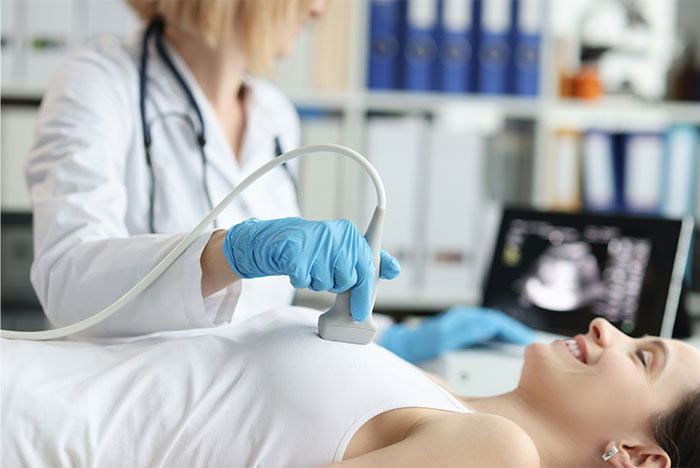 Doctor performing breast ultrasound on a smiling patient, highlighting symptoms that made people see a doctor for cancer.