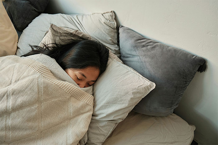 Woman lying in bed looking fatigued, illustrating symptoms that made people see a doctor for cancer diagnosis.