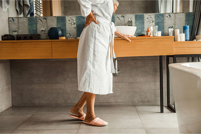 Person in a bathrobe holding their lower back, representing symptoms that made people see a doctor for cancer.