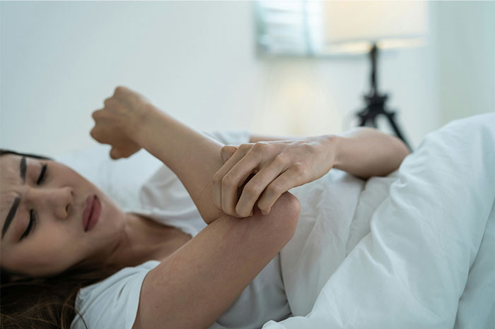 Woman in bed holding her elbow in pain, illustrating symptoms that made people see a doctor for cancer diagnosis.