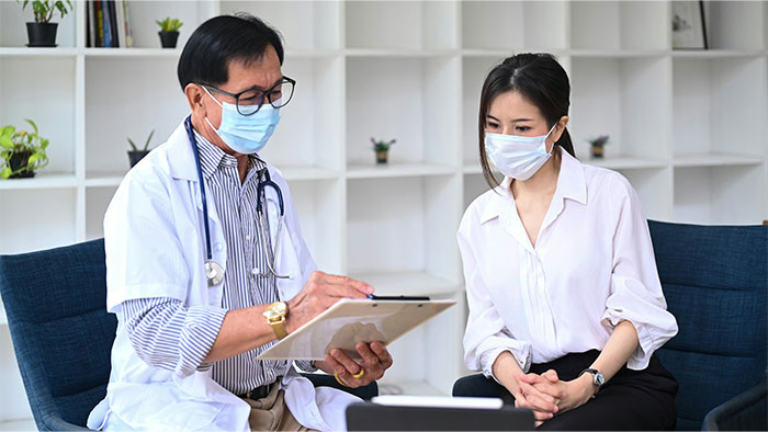 Doctor in white coat discussing symptoms with patient wearing a mask, focusing on warning signs that led to cancer diagnosis.