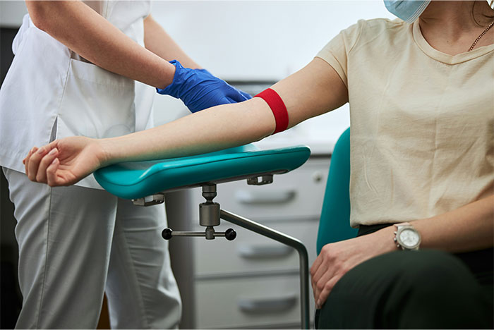 Patient wearing mask having blood drawn by nurse in medical clinic representing symptoms that made people see a doctor for cancer.