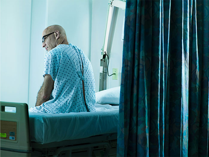 Patient in hospital gown sitting on bed, representing symptoms that led to cancer diagnosis and doctor visits.